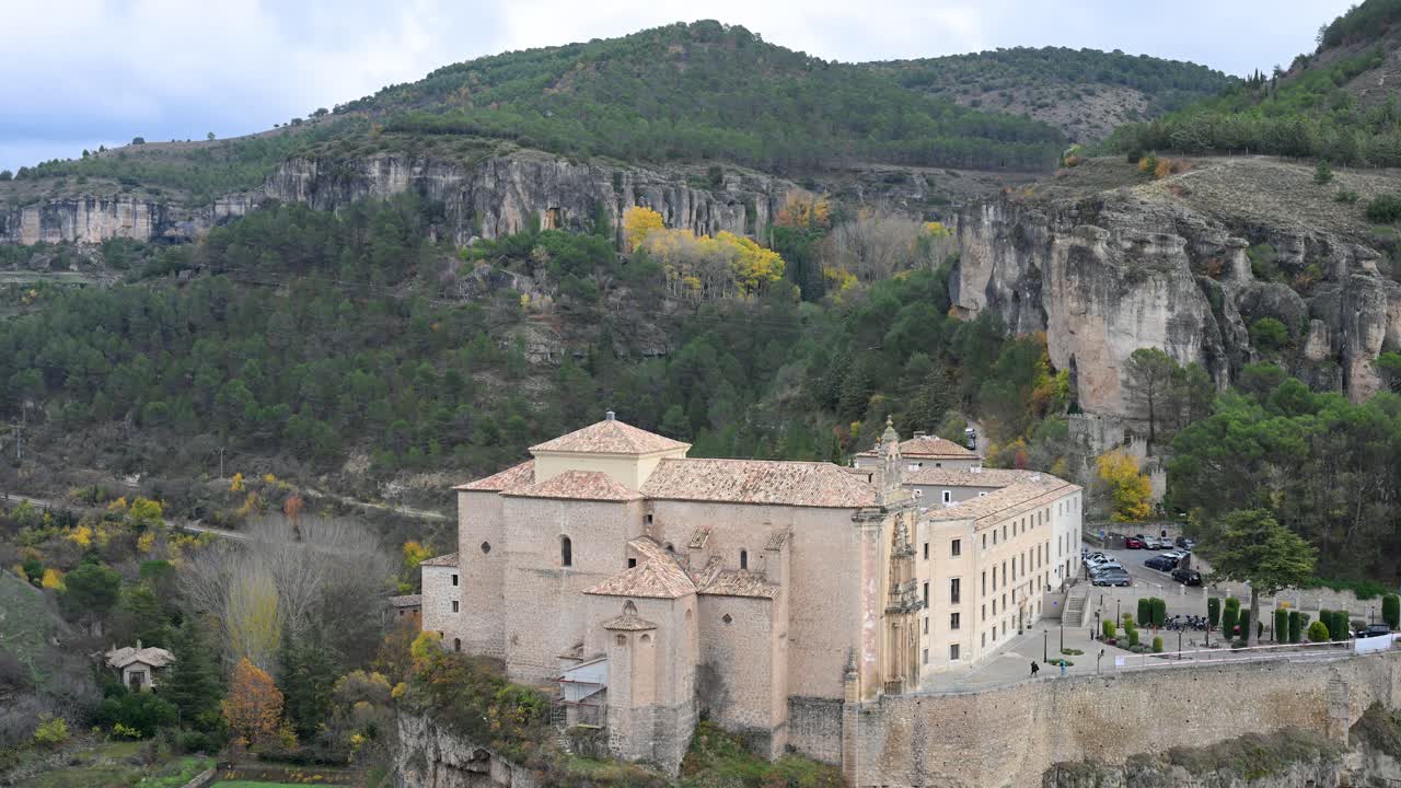 CUENCA, SPAIN - The historic Parador de Cuenca, a former convent, is seen perched on a cliff, surrounded by the dramatic hills and autumn foliage of the Spanish landscape.