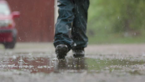 Cámara-Lenta,-Las-Piernas-De-Un-Niño-Caminan-A-Través-De-Un-Charco-Bajo-La-Fuerte-Lluvia