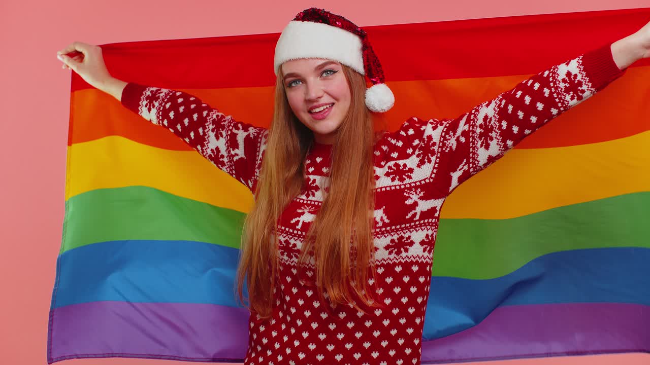 크리스마스 스웨터를 입은 소녀가 무지개  ⁇ 발과 포즈를 취하여 퍼레이드 관용 동성 결혼을 축하합니다.