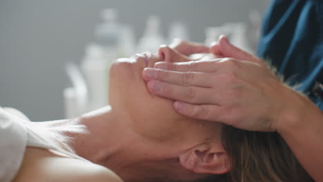 model lies relaxed with eyes closed while beauty technician gently smooths massage cream in circular motion across cheeks and forehead, creating luminous hydrated skin and tranquil spa ambiance
