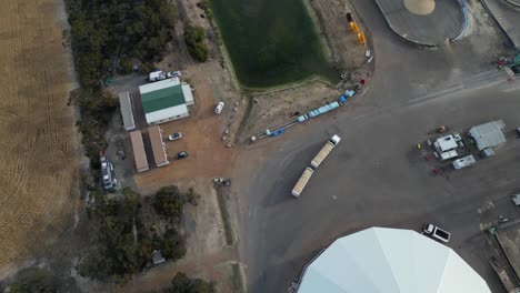 muestra aérea de arriba hacia abajo de un camión de carga industrial que llega a una granja con un gran silo de almacenamiento en australia