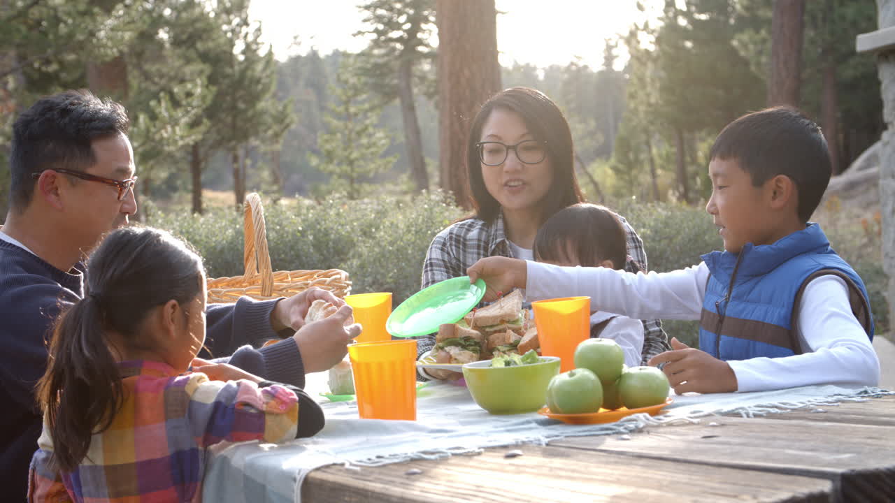 아시아 가족 이 야외 테이블 에서 피크닉 음식 을 나누고 있다
