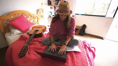 young girl typing on her laptop sitting on bed