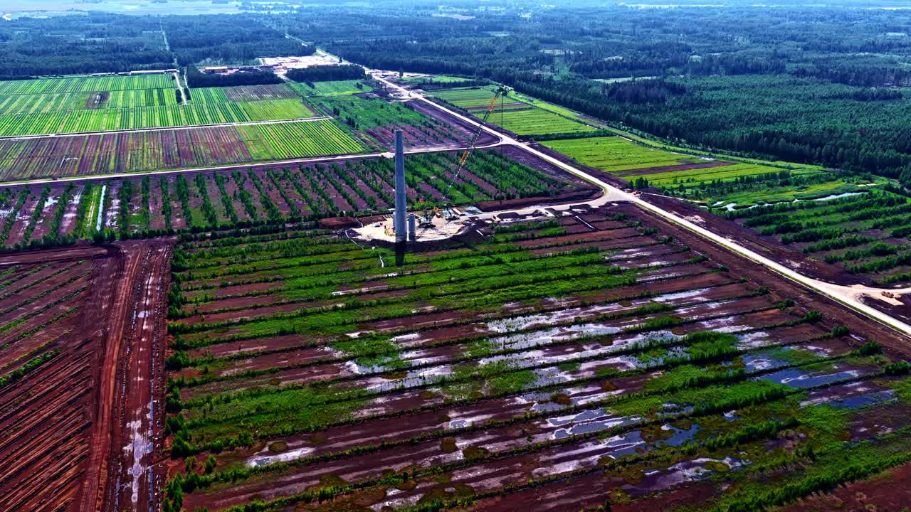 Wide angle drone view of chimneys in construction by using cranes in between a lush, green field