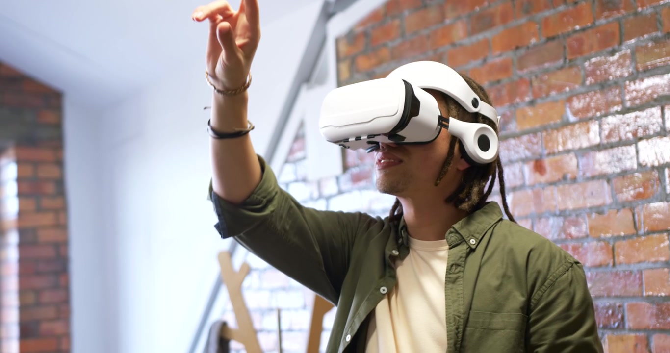 Uomo che guarda in alto e sorride, che si allunga, che pizzica, testando un'app usando un visore VR bianco in un loft.