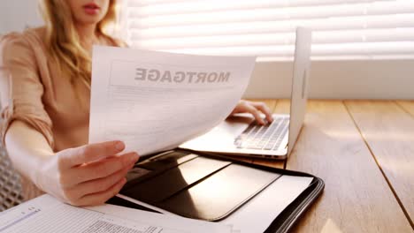 woman looking at bill while using laptop