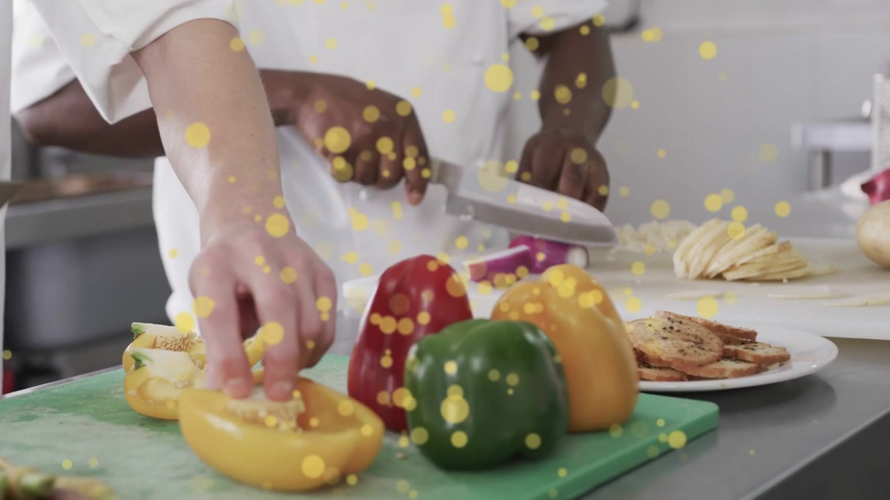 Lo chef a sinistra posiziona il coltello e toglie il torsolo a un peperone giallo, mentre lo chef a destra affetta una cipolla, preparando la mise en place.