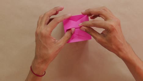 hands folding small pink box with intricate details on neutral background