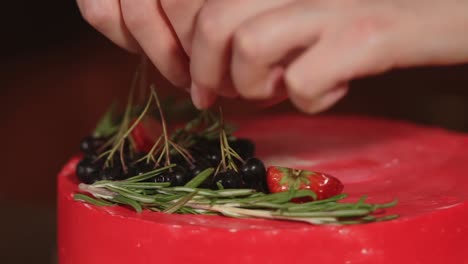 decorating a red velvet cake with berries and fresh herbs