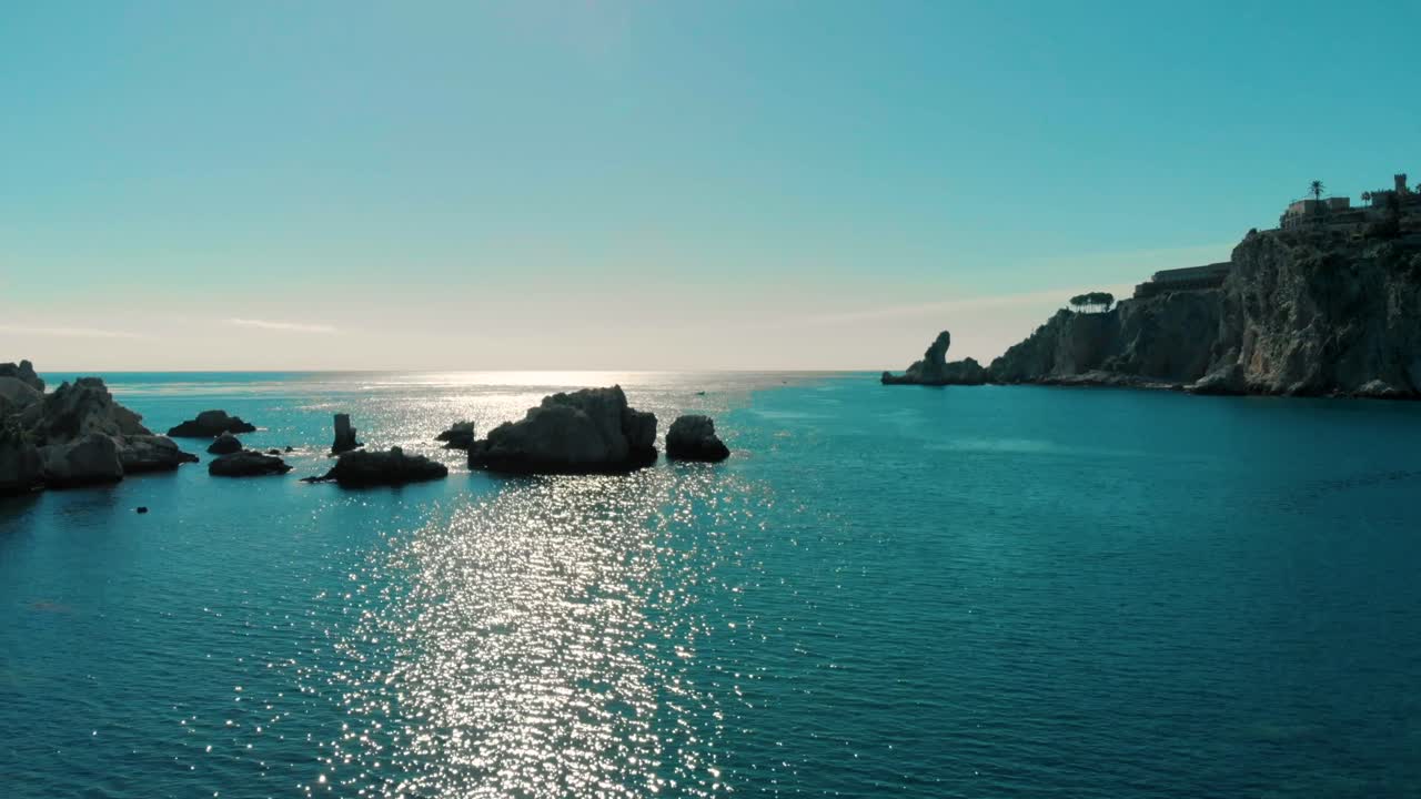 Aerial drone view of rocky coastline and calm blue sea in Canada with bright sunlight reflecting on water, showing peaceful ocean horizon and cliffs with clear sky in scenic natural environment