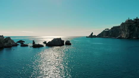aerial drone view of rocky coastline and calm blue sea in canada with bright sunlight reflecting on water, showing peaceful ocean horizon and cliffs with clear sky in scenic natural environment