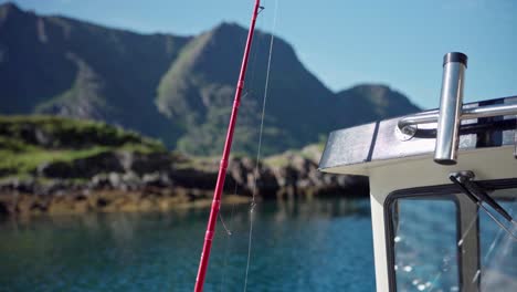 fishing rod at sailing ship on calm river passing through lush mountains during sunny day in norway
