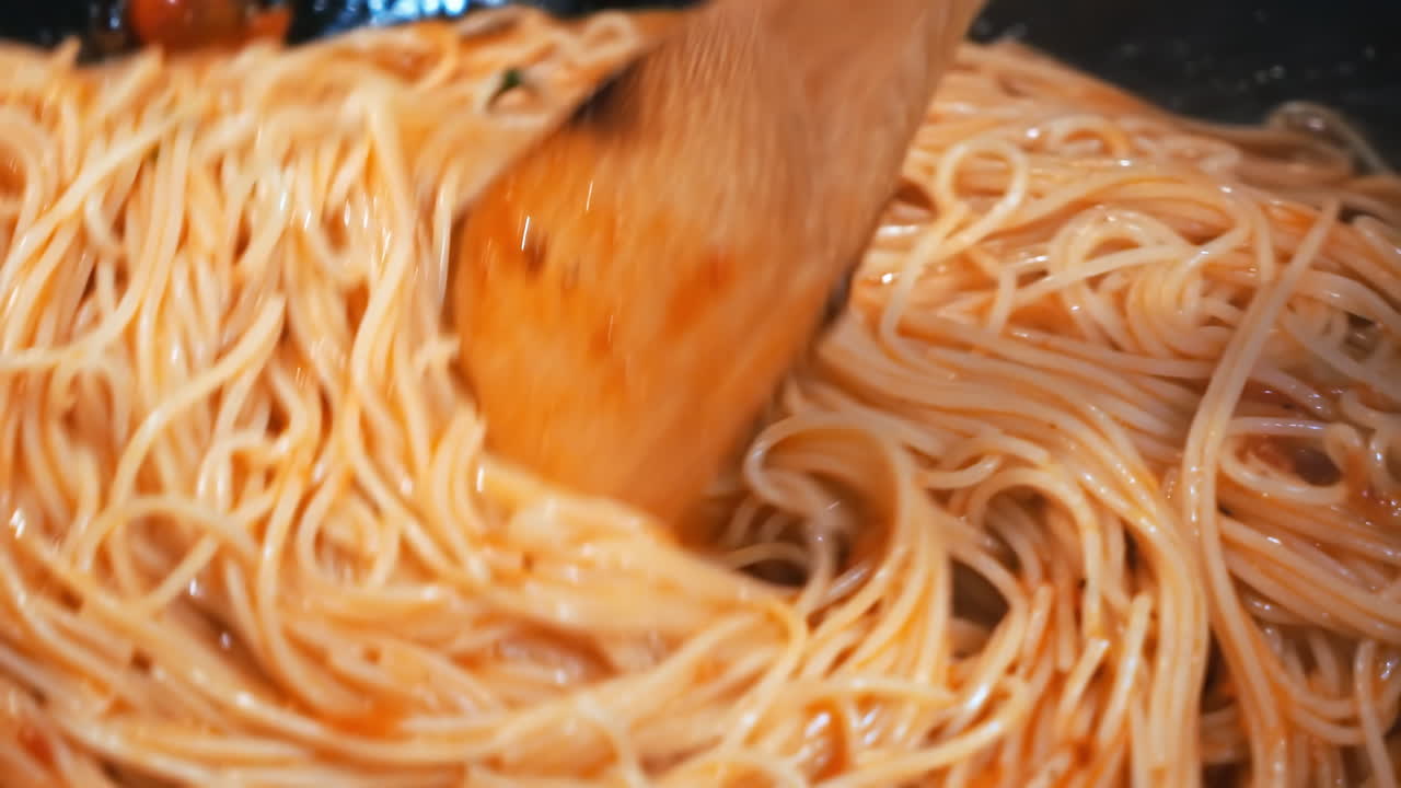 A man is stirring spaghetti with sausage in a pan on a stove