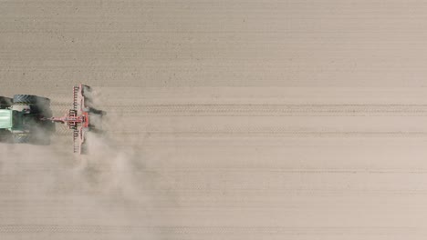 aerial view of plowed field with tractor sowing seeds of wheat, agricultural theme, farm tractor and seeder planting crops on a field on sunny spring day, birdseye drone dolly shot moving left