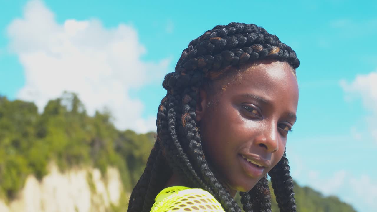 땋은 머리를 한 소녀가 돌아서서 파란 하늘을 배경으로 미소 짓는 동안