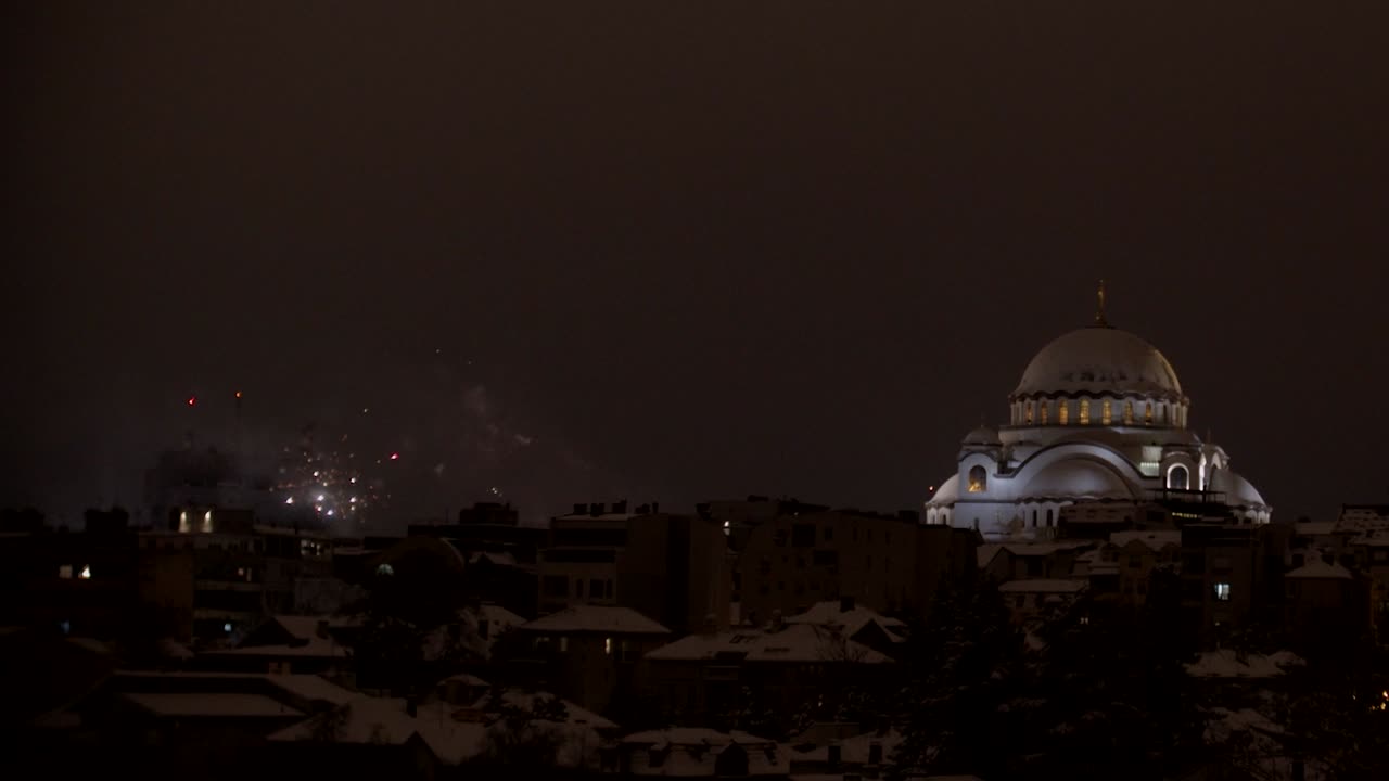 Panning shot of fireworks in the sky next to an impressive orthodox christian church on the top of a city scape.