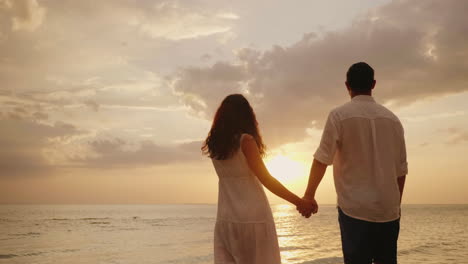 Young-Loving-Couple-Holding-Hands-Stand-In-The-Water-And-Look-At-The-Sunset-Over-The-Sea-4k-Video