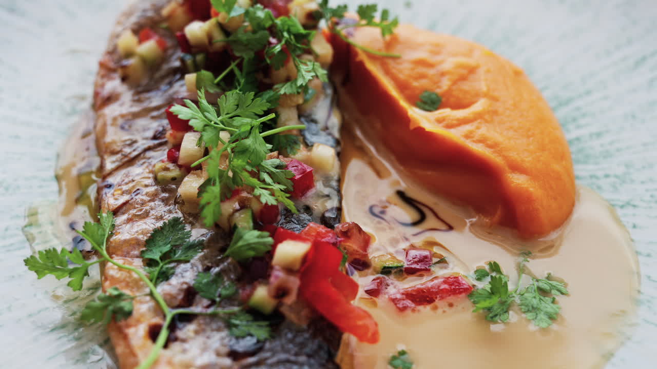 Close up of grilled fish with a sweet potato puree and a sauce on a white plate on a table at a restaurant