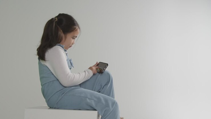 Scatto in studio di giovane ragazza nello spettro ASD che gioca al telefono cellulare su sfondo bianco 1.