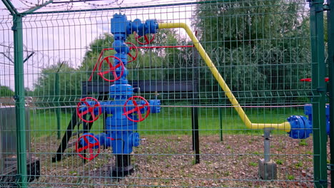 a "christmas tree" valve assembly stands at a natural gas wellhead or storage injection point, located within a high-security fence with warning signs at an industrial facility in latvia