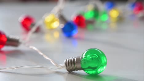 capturado en una vista de cerca contra una superficie blanca, una agrupación de luces de navidad centradas alrededor de una bombilla verde distinta, en un fondo de bombillas azules, rojas, amarillas y verdes