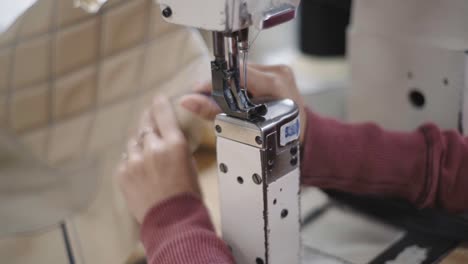 primo piano delle mani di un operaio specializzato che passa il tessuto attraverso una macchina da cucire, all'interno dell'officina