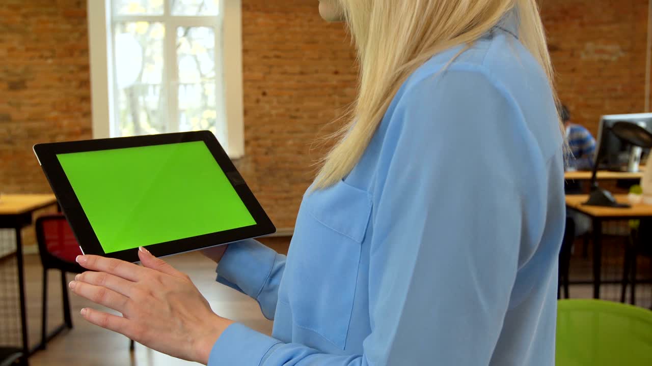 un primer plano de una mujer joven y atractiva usando una tableta negra con pantalla verde en una oficina moderna.