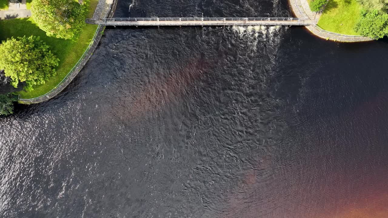 Drone captures hydroelectric dam, flowing river, green landscape, and infrastructure in bright daylight