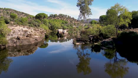 Vuelo-Aéreo-Sobre-Un-Río-Tranquilo-Con-Hermosos-Reflejos-Paisajísticos-De-La-Sierra-De-Andújar.