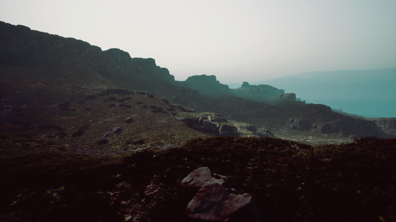 Scenic view of rugged cliffs beside calm waters at dawn on a foggy morning