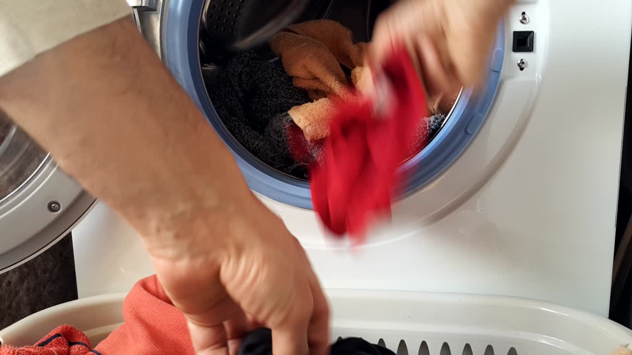 개방된 문으로 세탁기 손으로 더러운 옷을 드럼에 던집니다.