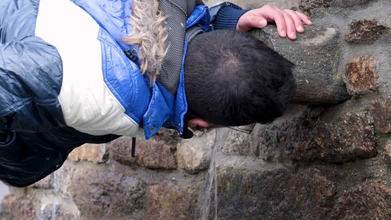 bebiendo agua del chorro de agua de una fuente de piedra, video al aire libre