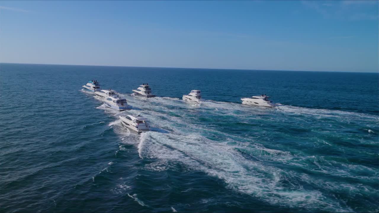 Wide daytime shot of modern motor yachts cruising together on calm blue ocean under a bright sky, their foamy wakes creating an aspirational feeling of luxury travel, wealthly luxurious lifestyle