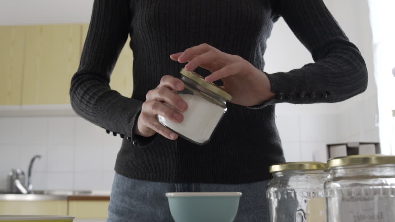 tiro medio de cámara lenta como una mujer abriendo un frasco de vidrio en la cocina azúcar blanca
