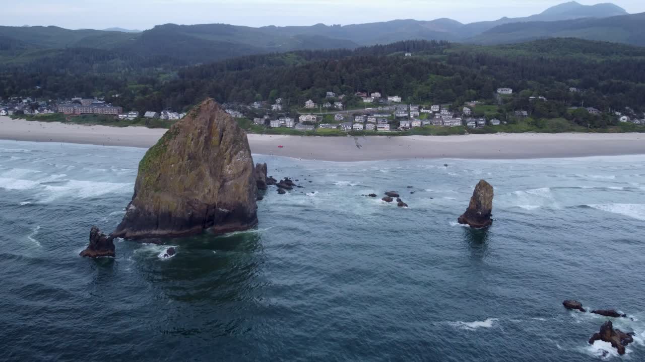 Sun illuminating the colors of Haystack Rock, the ocean, the forest, the houses, and hotels at sunset in Cannon Beach, Oregon. This 4K drone footage shows the natural beauty of the Oregon coastline.