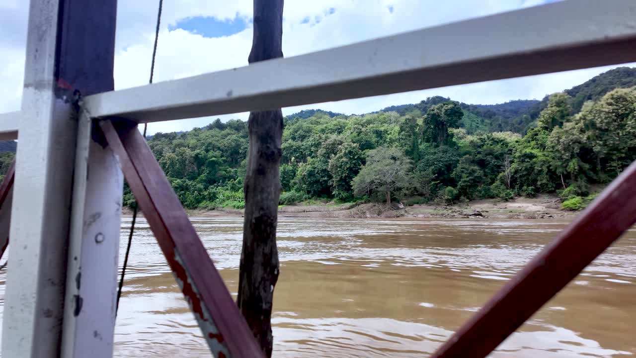 Mekong river scene with a boat railing framing lush forest riverbank and calm water