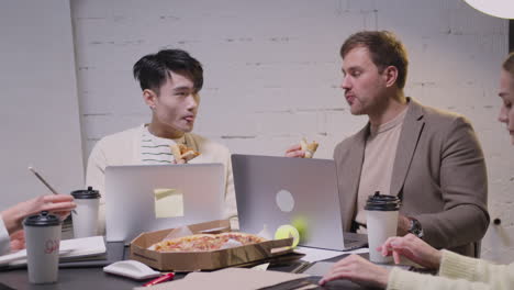 dos colegas multiétnicos comiendo pizza durante una reunión de equipo en la sala de juntas