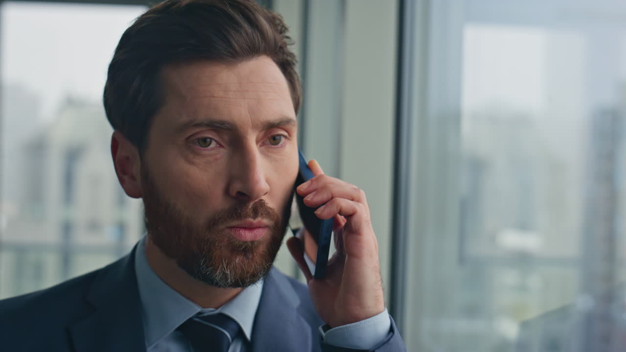 Confident businessman speaking cellphone at panoramic window office closeup