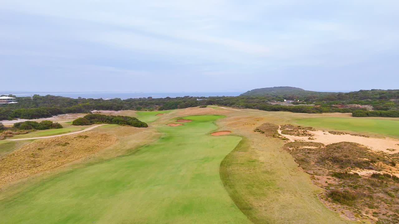 Aerial footage of a lush golf course in Barwon Heads, showcasing vibrant greens and sand traps under a cloudy sky