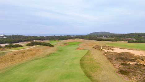 aerial footage of a lush golf course in barwon heads, showcasing vibrant greens and sand traps under a cloudy sky