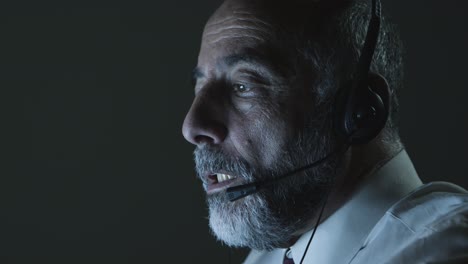 hombre maduro con auriculares trabajando en una oficina oscura