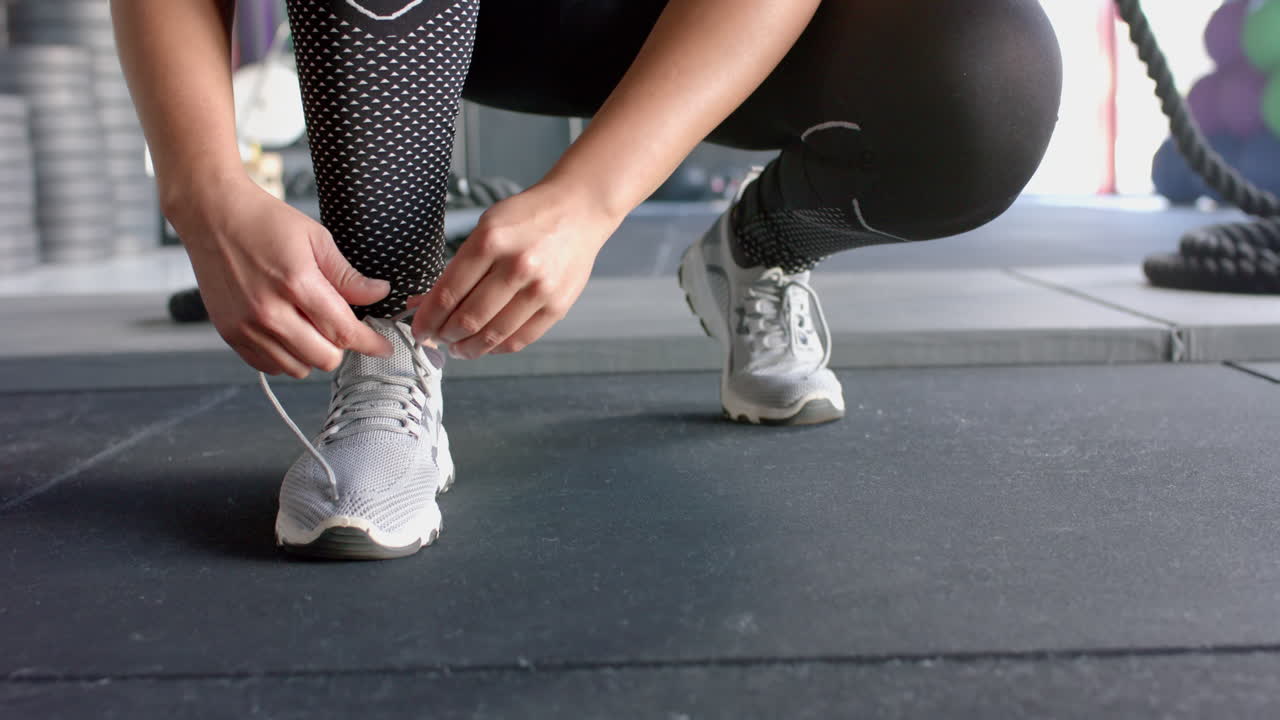 Donna che si allaccia le scarpe, preparandosi per l'allenamento in palestra, indossa scarpe sportive.