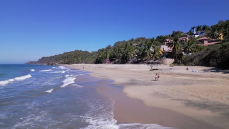 2 mujeres caminan por la playa de sayulita méxico con olas rompiendo cerca de ellas vistas desde el punto de vista de un dron aéreo