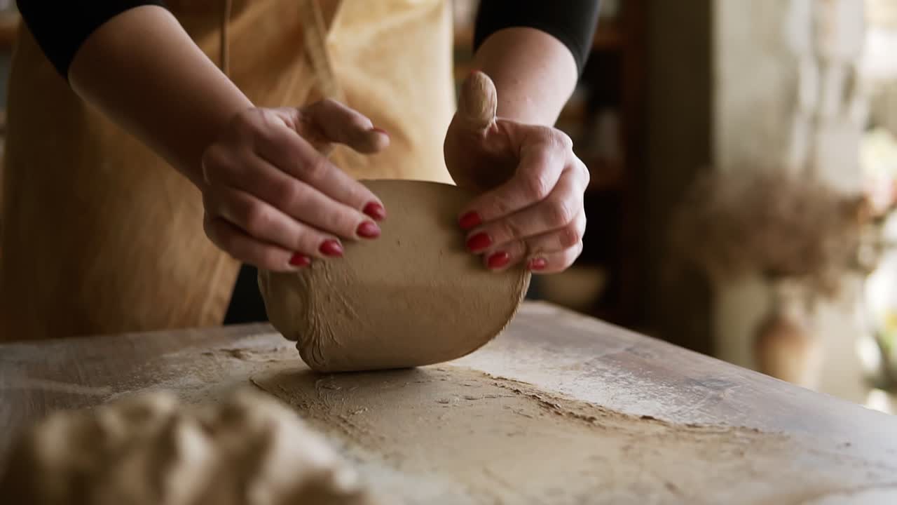 крупным планом кадры женских рук с красивым красным маникюром, держащих глину и разминающих ее на рабочей поверхности