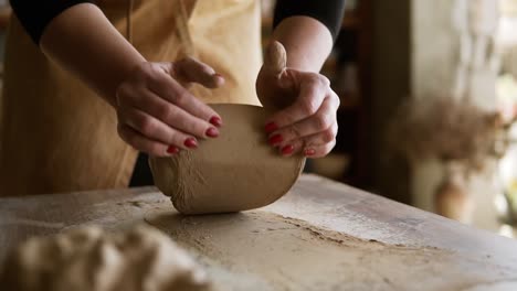 images en gros plan de mains féminines avec une belle manucure rouge tenant de l'argile et la pétrissant sur un plan de travail