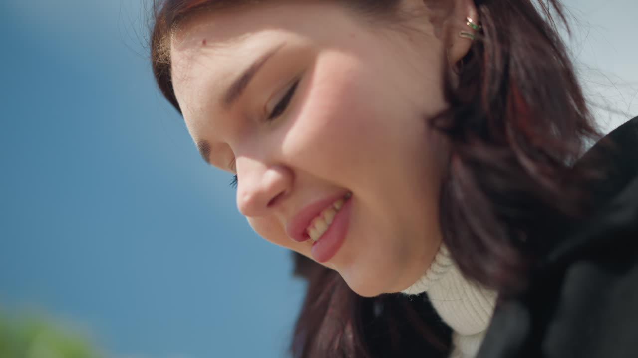 웃는 여자의 클로즈업, 눈에 보이는 귀걸이, 바람에 부드럽게 흔들리는 머리카락, 빛나는 행복, 부드러운 자연 조명과 함께 밝은 배경에