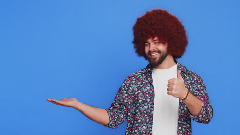 joven mostrando los pulgares hacia arriba y señalando a la izquierda en el espacio en blanco lugar para su logotipo de publicidad