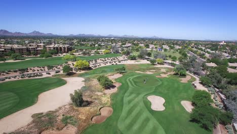 El-ángulo-De-Altura-Aérea-Se-Aleja-De-Los-Cuatro-En-El-Green-Para-Revelar-La-Calle,-Las-Trampas-De-Arena-Y-El-Concepto-áspero-De-Scottsdale,-Arizona:-Ejercicio,-Turismo,-Verde