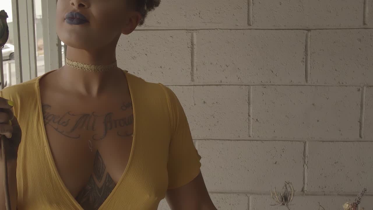 Woman with tattoos in a yellow dress holding and looking at a withered rose