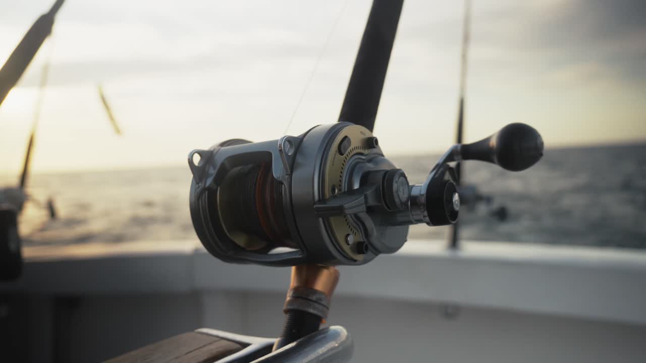 Detailed close-up of a fishing reel on a boat rod with the ocean fading in the distance.